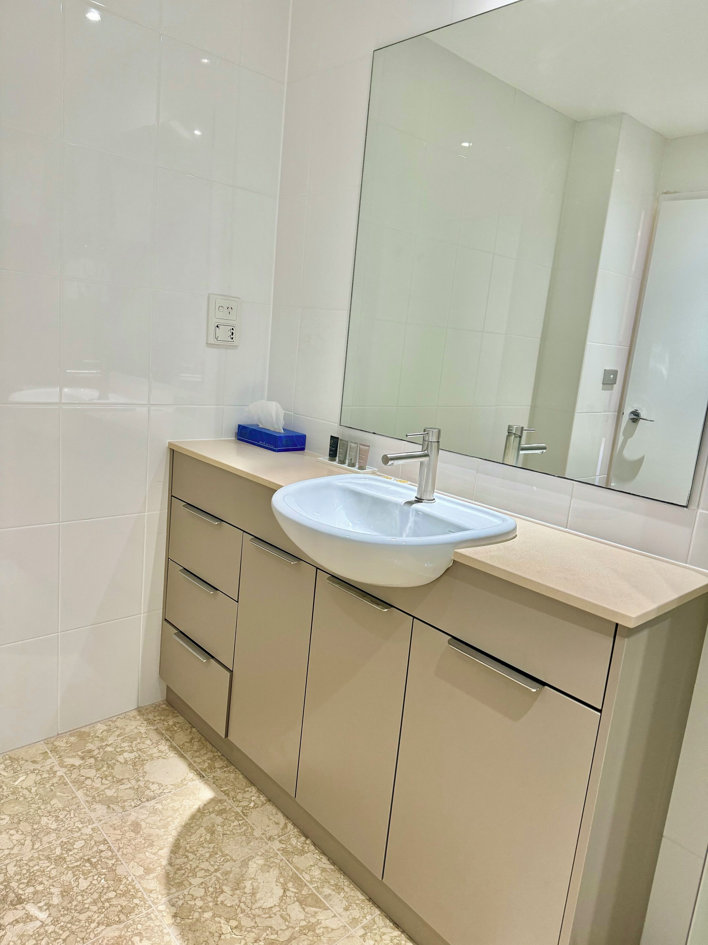 Un baño moderno con un lavabo blanco, muebles color beige y un espejo grande.