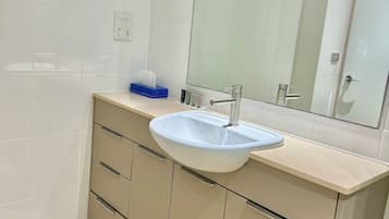 Un baño moderno con un lavabo blanco, muebles color beige y un espejo grande.