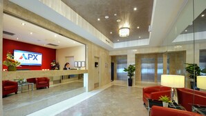A hotel reception area with a reception desk, red seating, a chandelier, and elevators. - APX Darling Harbour (Sydney)
