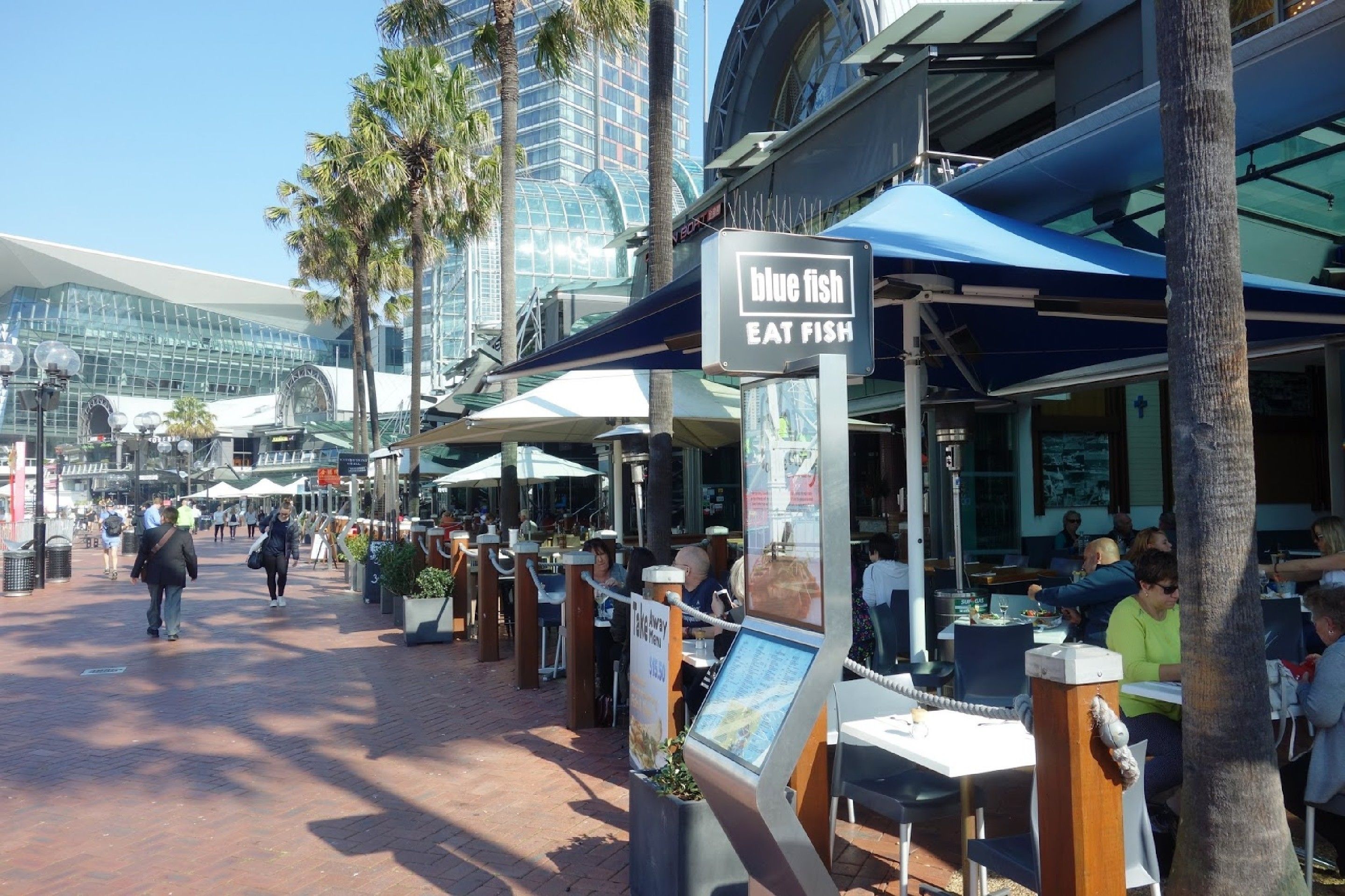 A restaurant named 'Blue Fish' with outdoor seating and a view of a modern building in the background.