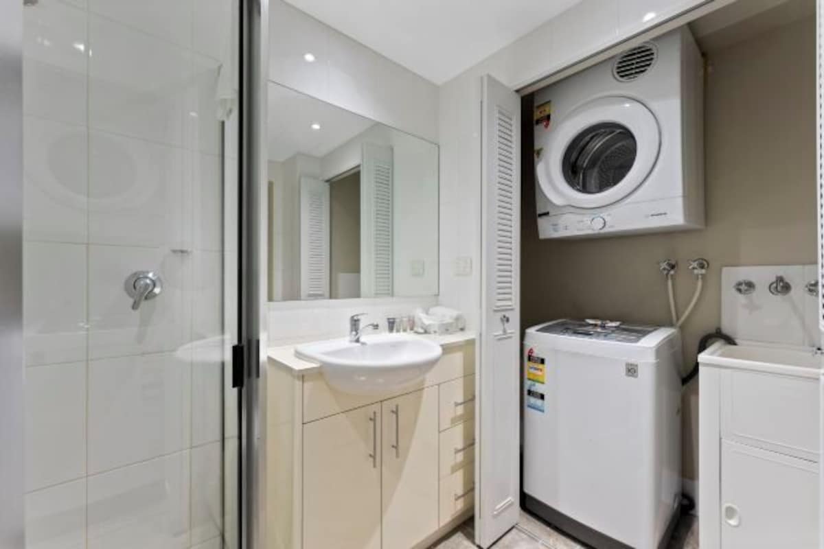 Un baño pequeño con cabina de ducha de vidrio, un lavabo, un espejo y una lavadora integrada.