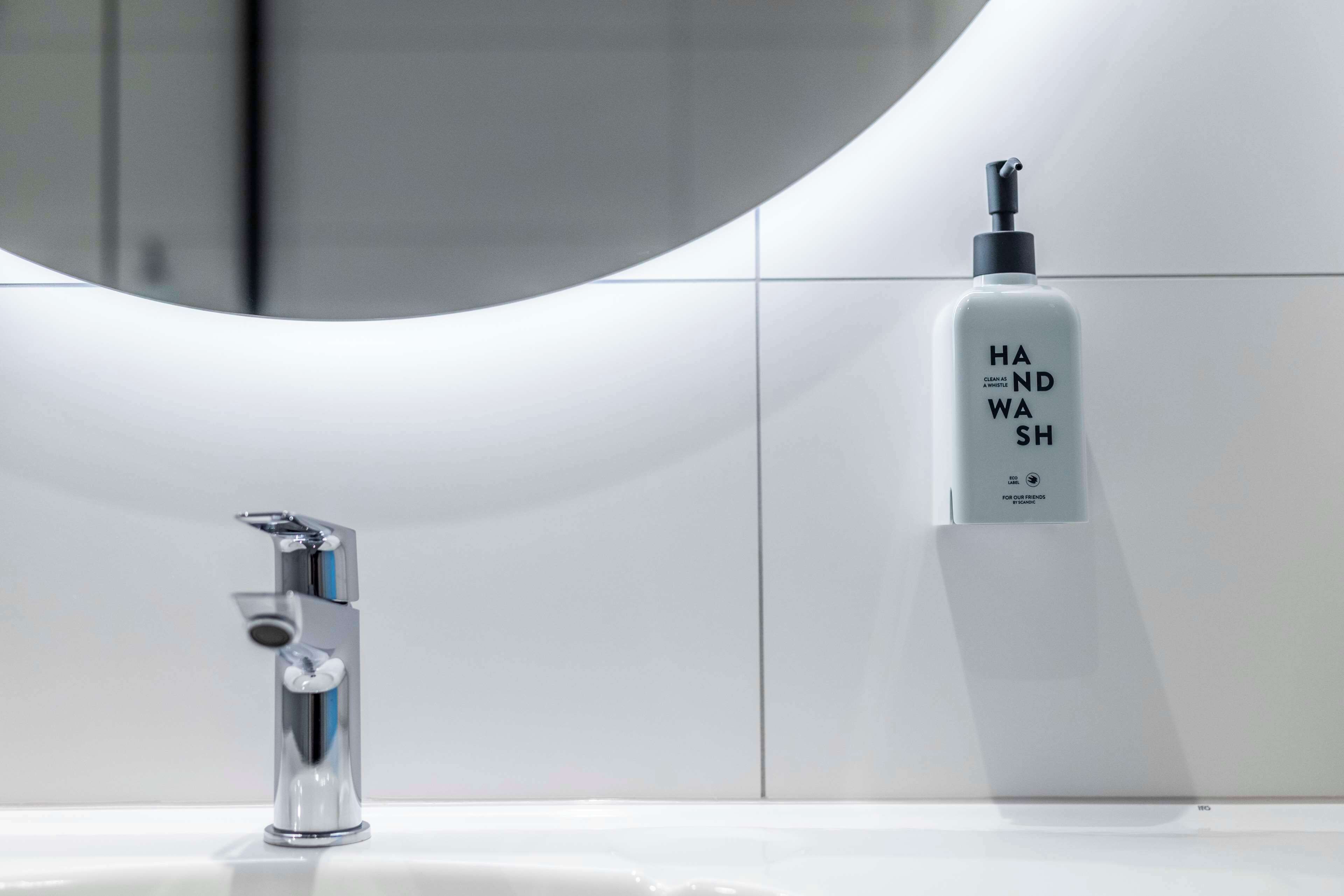 Un baño moderno con grifo de cromo, un lavabo blanco y un dispensador de jabón.