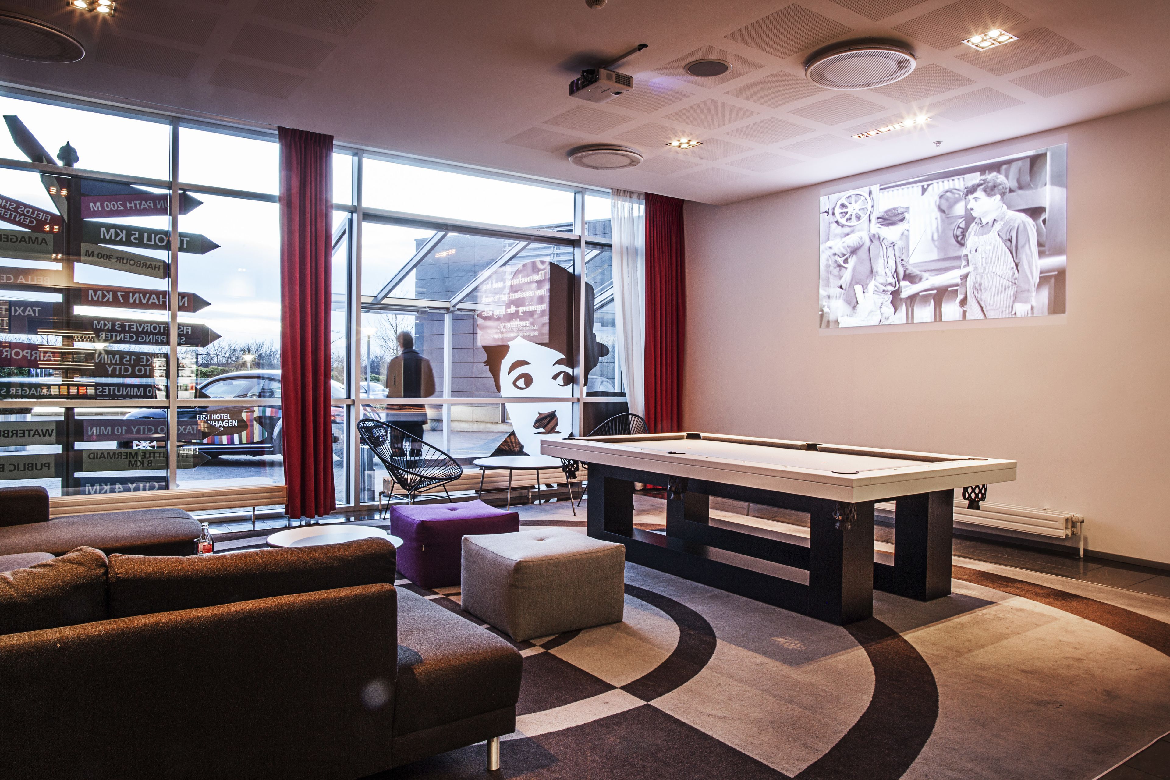 A pool table in a modern lounge area with a large window and directional signpost.