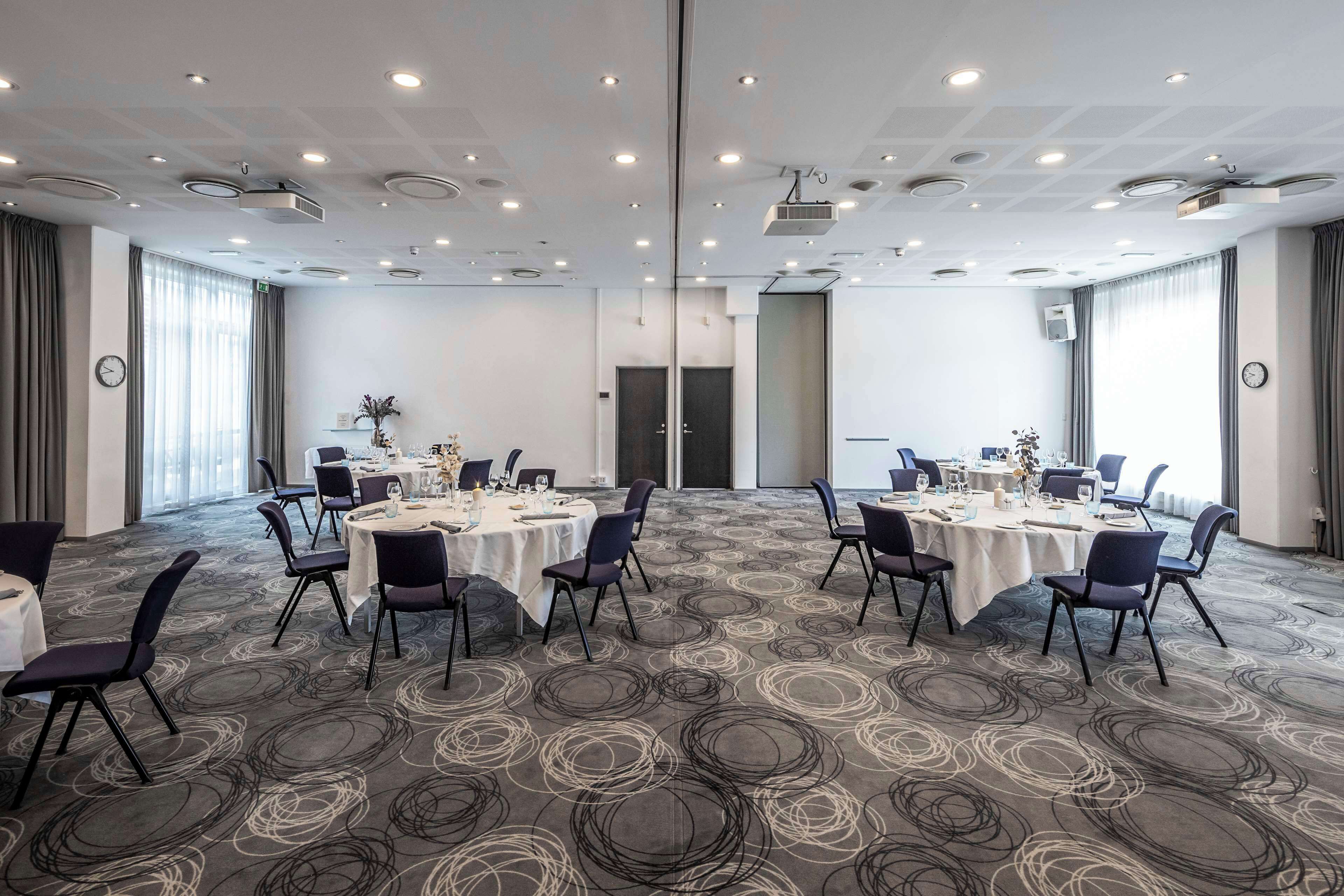 Una sala conferenze con tavoli rotondi, sedie e pavimento rivestito di moquette.
