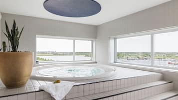 Une salle de bain moderne avec une grande baignoire, une plante en pot et une vue sur un plan d’eau grâce à de grandes fenêtres.