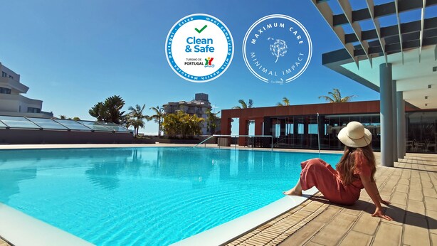 A pool area with a person sitting by the pool, a modern building with glass windows, and logos indicating 'Clean & Safe' and 'Maximum Care'. - The Views Monumental (Funchal)
