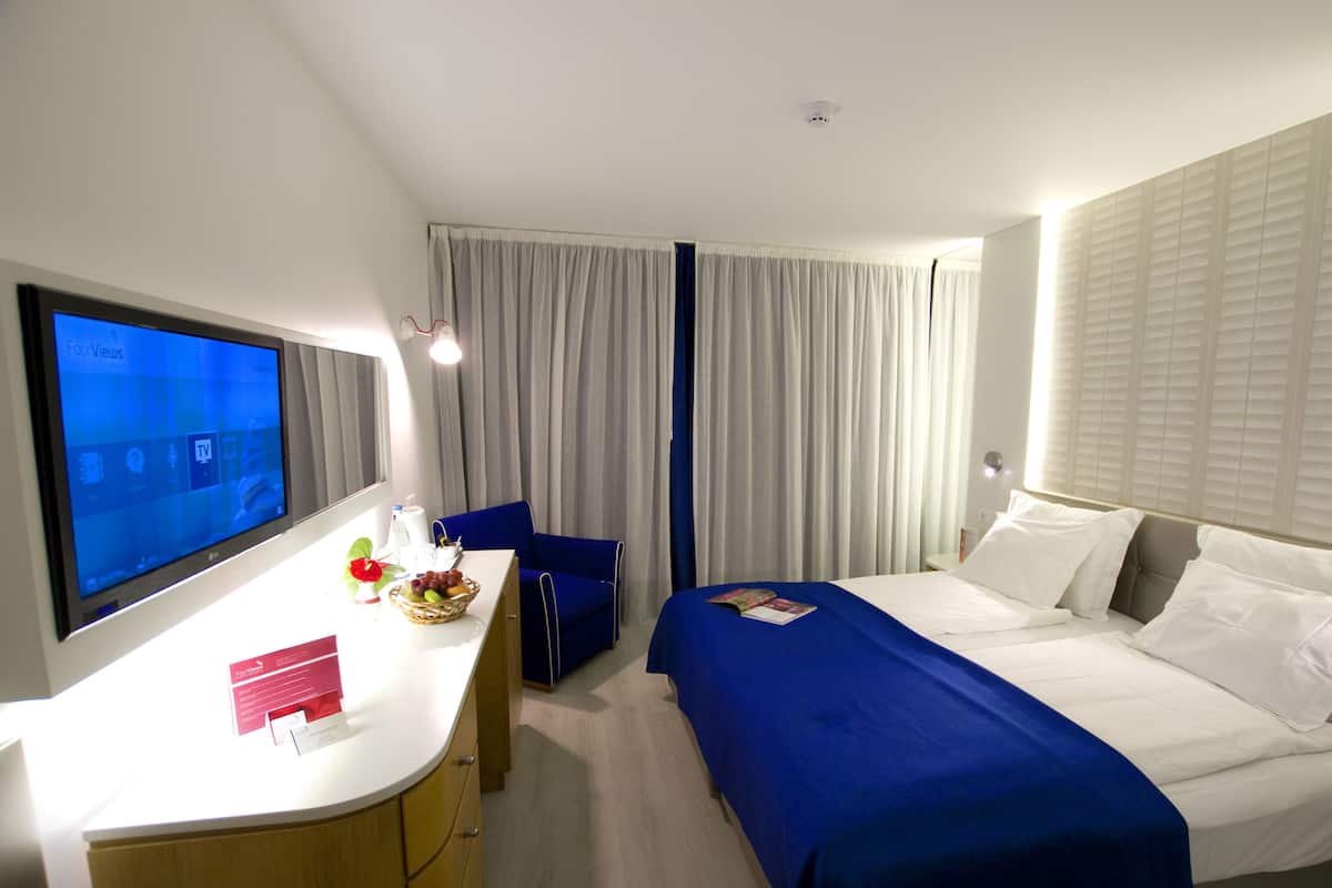 A hotel room with a bed, a desk, a chair, and a television.