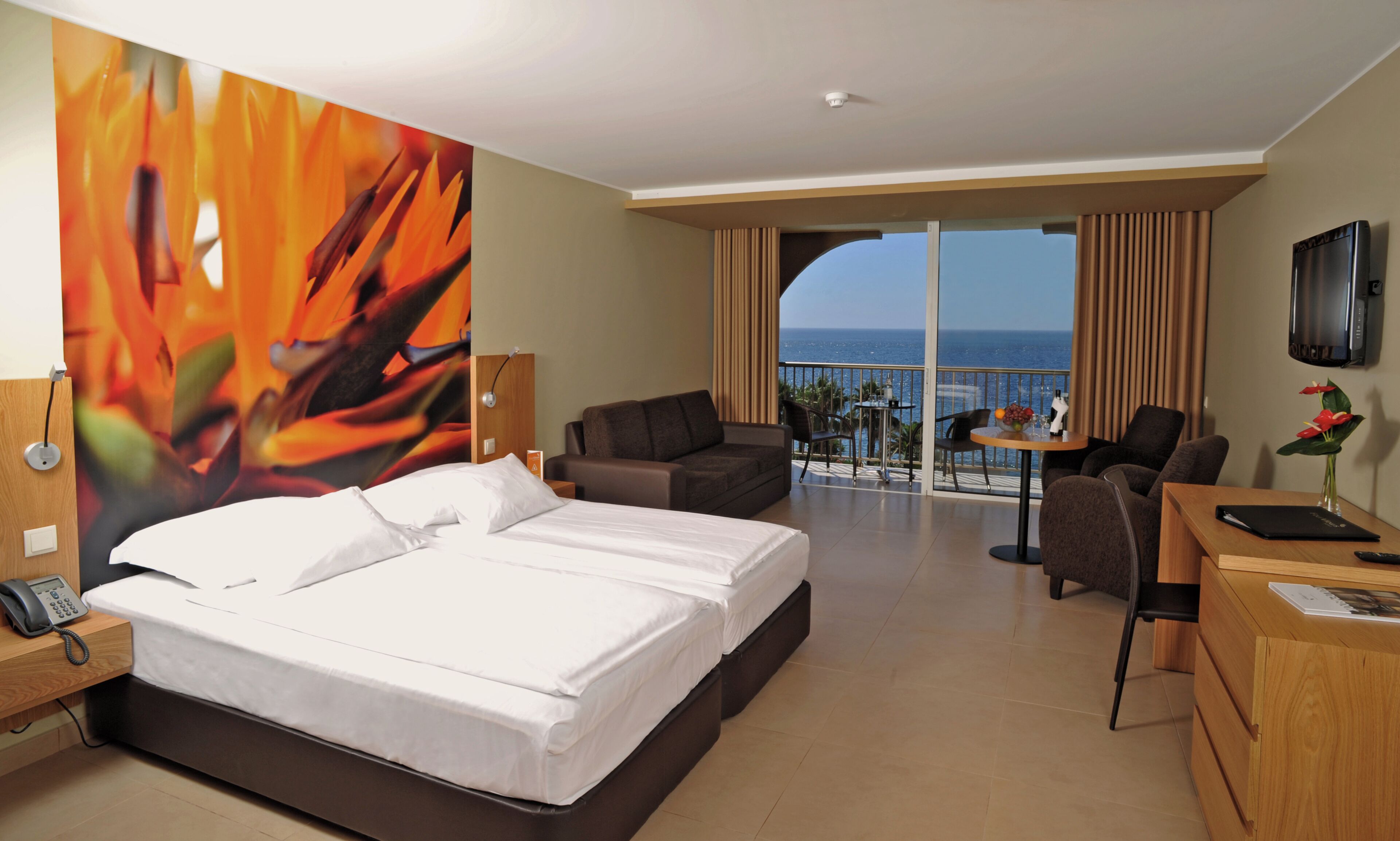 Une chambre d’hôtel équipée d’un lit, d’un bureau, d’une chaise, d’une télévision et d’un balcon avec vue sur la mer.