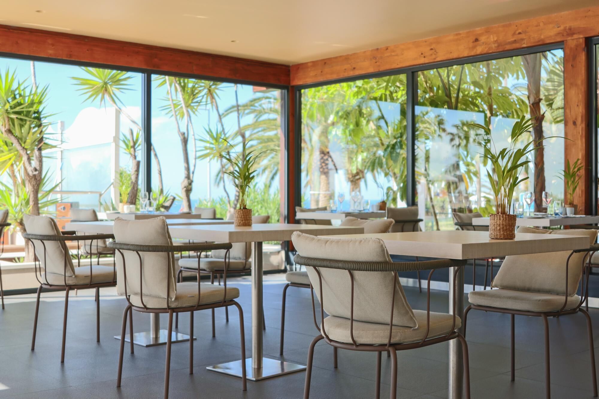 Un espace repas moderne avec de grandes fenêtres, des chaises en osier et des plantes en pot.