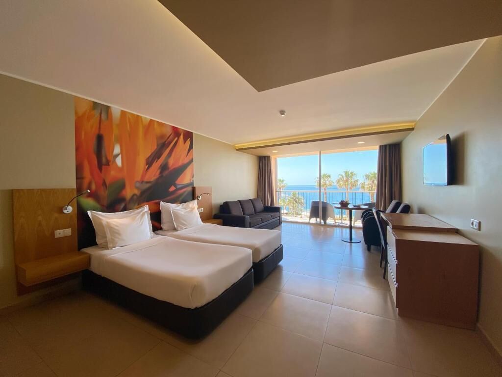 Une chambre d’hôtel avec deux lits, un bureau, une chaise, un canapé, une télévision et un balcon avec vue.