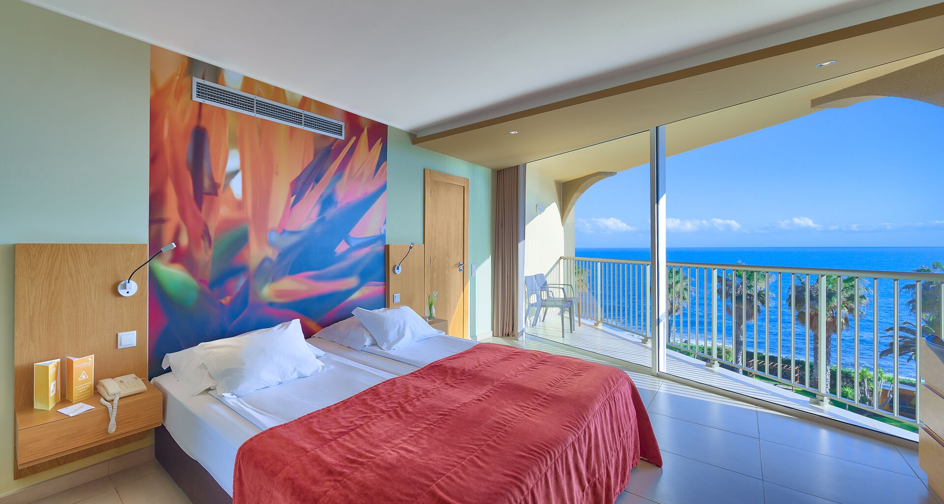 Une chambre d’hôtel avec un grand lit, une vue sur l’océan et un balcon doté d’une balustrade.
