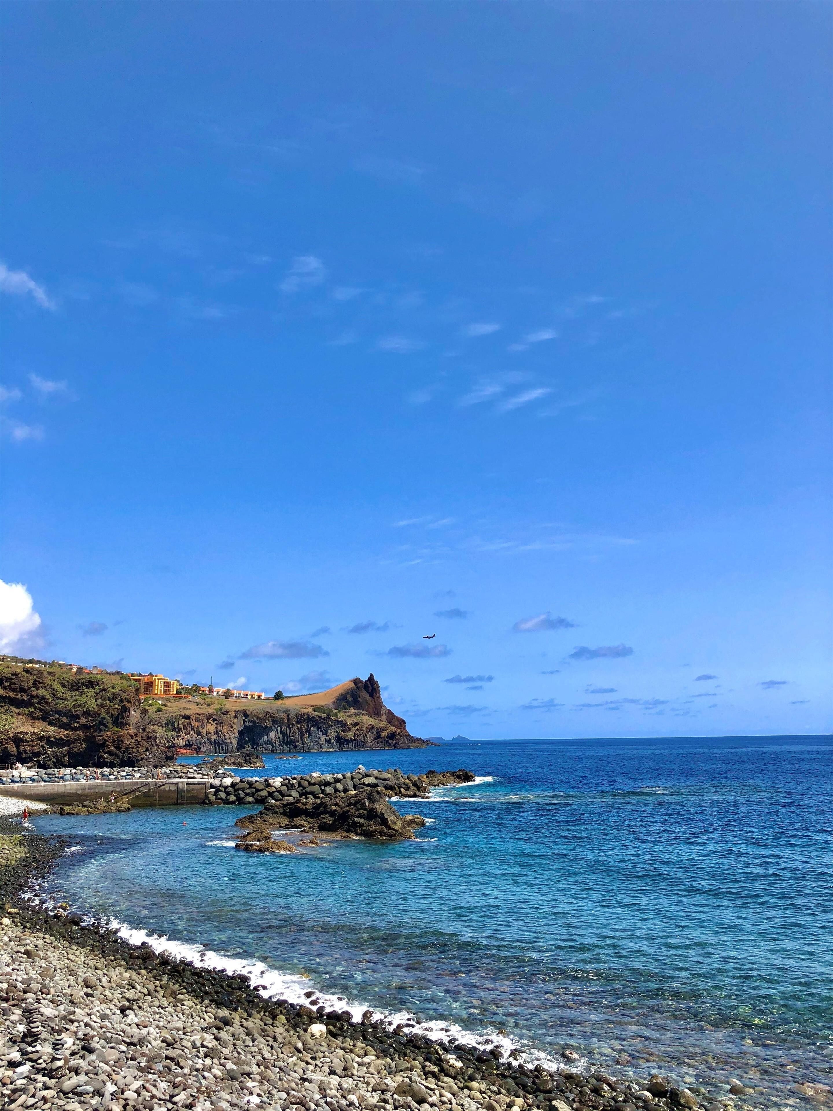 Un paisaje costero con aguas azules cristalinas, costa rocosa y un edificio distante en una colina.