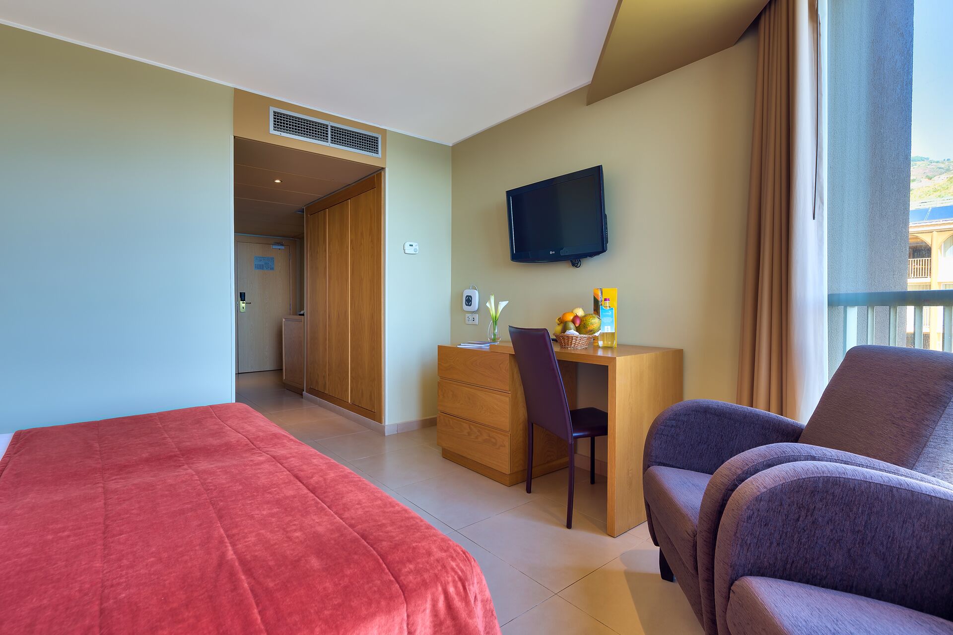 Habitación de hotel con cama, escritorio, silla, televisor y ventana con cortinas.