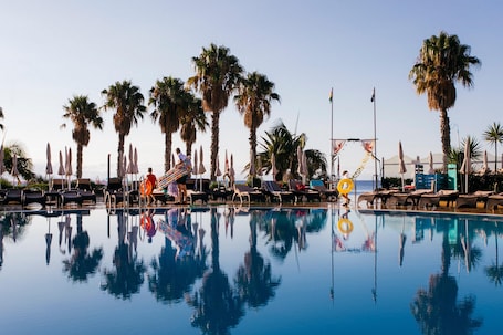 Una piscina al aire libre, sombrillas, sillones reclinables de piscina