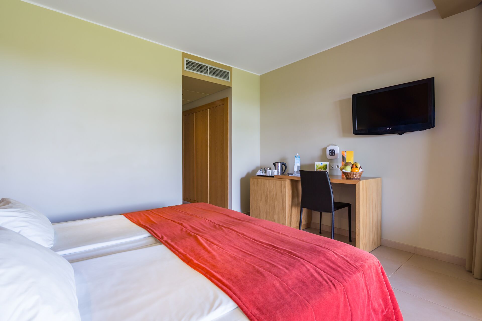 A hotel room with a bed, a desk with a chair, a television, and a small kitchenette area.
