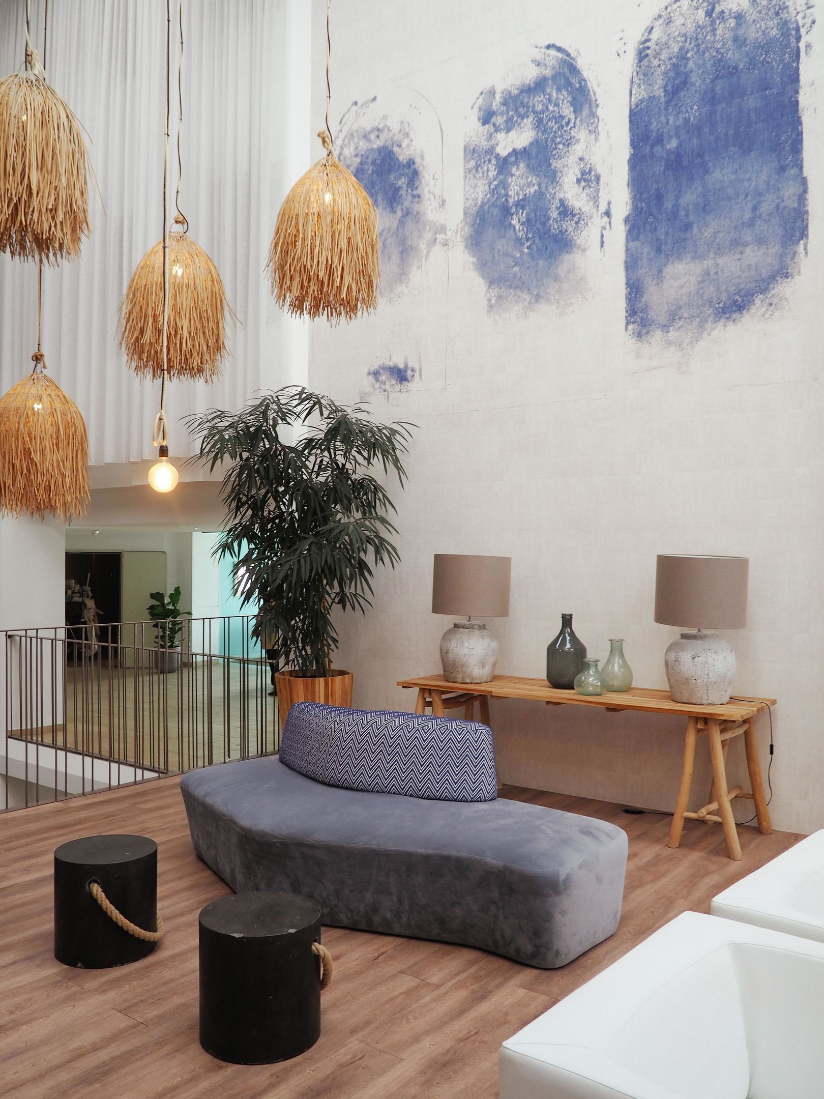 Ein modernes Wohnzimmer mit einer Couch, einer großen Kübelpflanze, hängenden Korbstühlen und einem Holztisch mit Lampen.