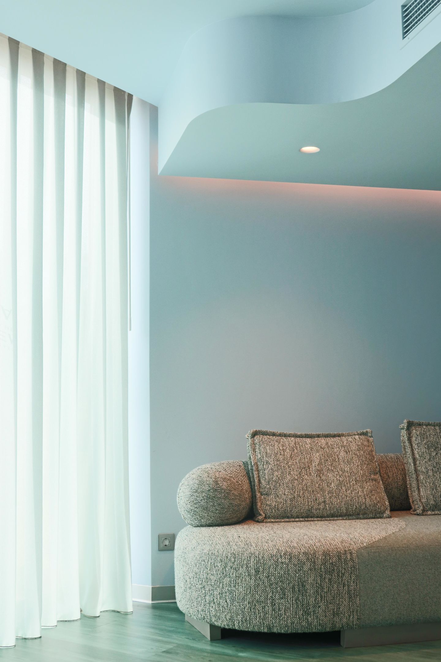 A modern living room with a sofa, a window with curtains, and a recessed ceiling light.