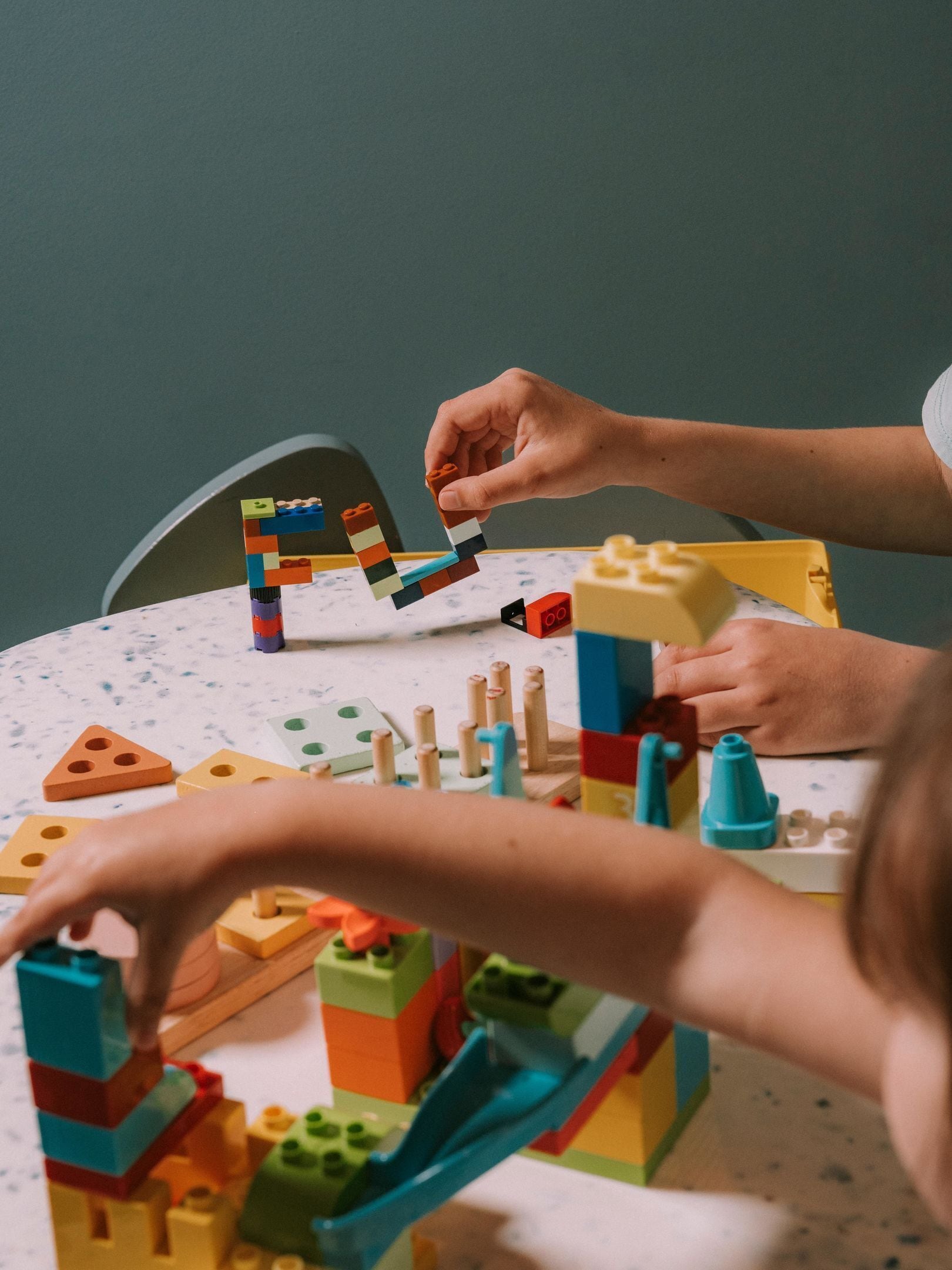 Een tafel met diverse bouwblokken en kinderhanden die ermee spelen.