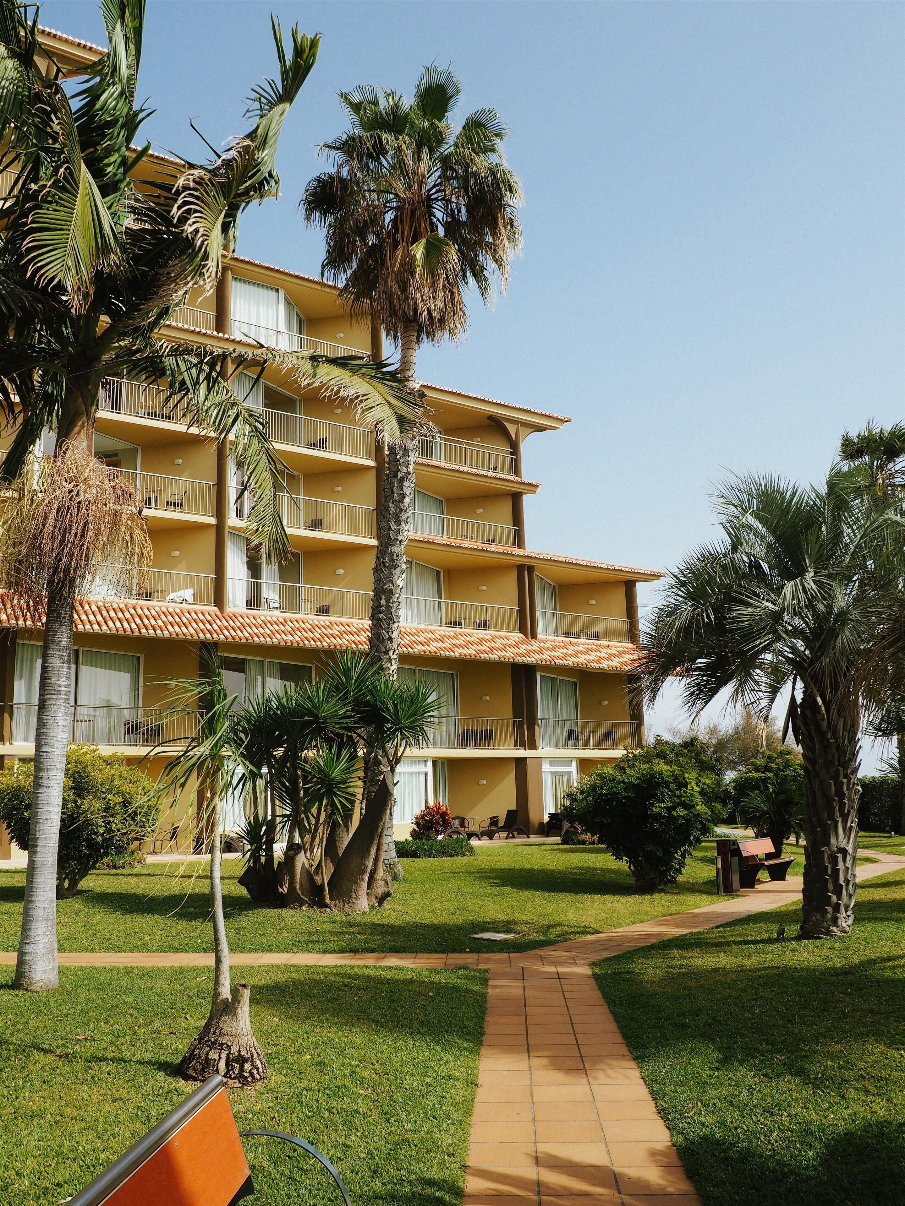 A multi-story hotel with balconies, palm trees, and a well-maintained lawn.