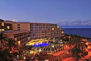 A hotel with a pool, multiple balconies, and a view of the sea.