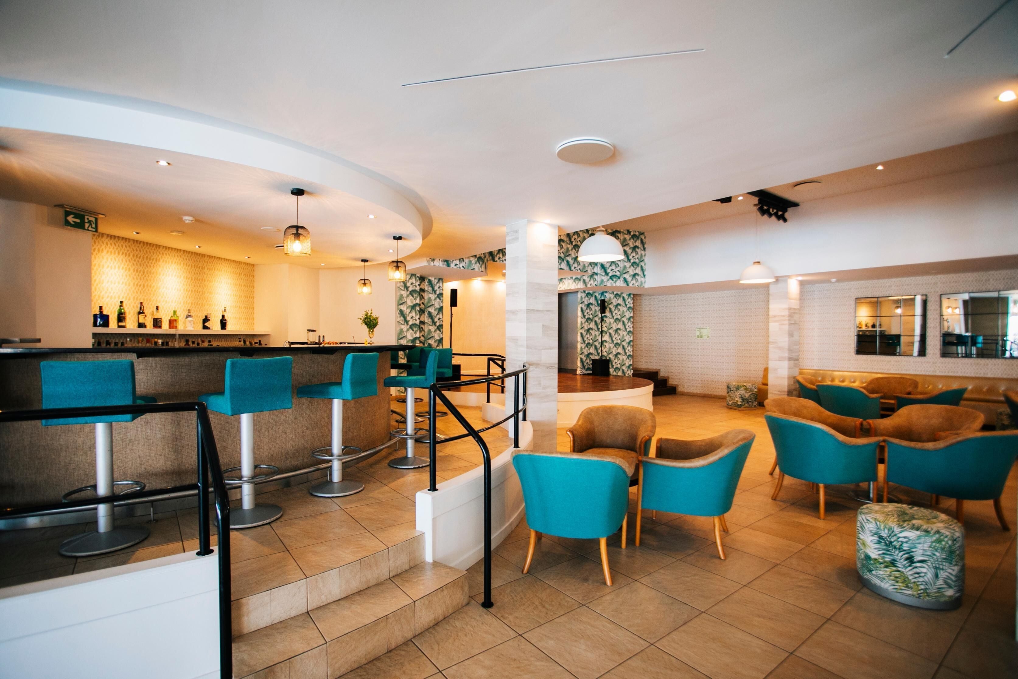 Eine moderne Bar mit Barhocker, einer Theke voller Flaschen und einer Sitzecke mit Sofas und Sesseln.