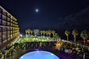 Hotel met een zwembad, terras en uitzicht op zee 's nachts.