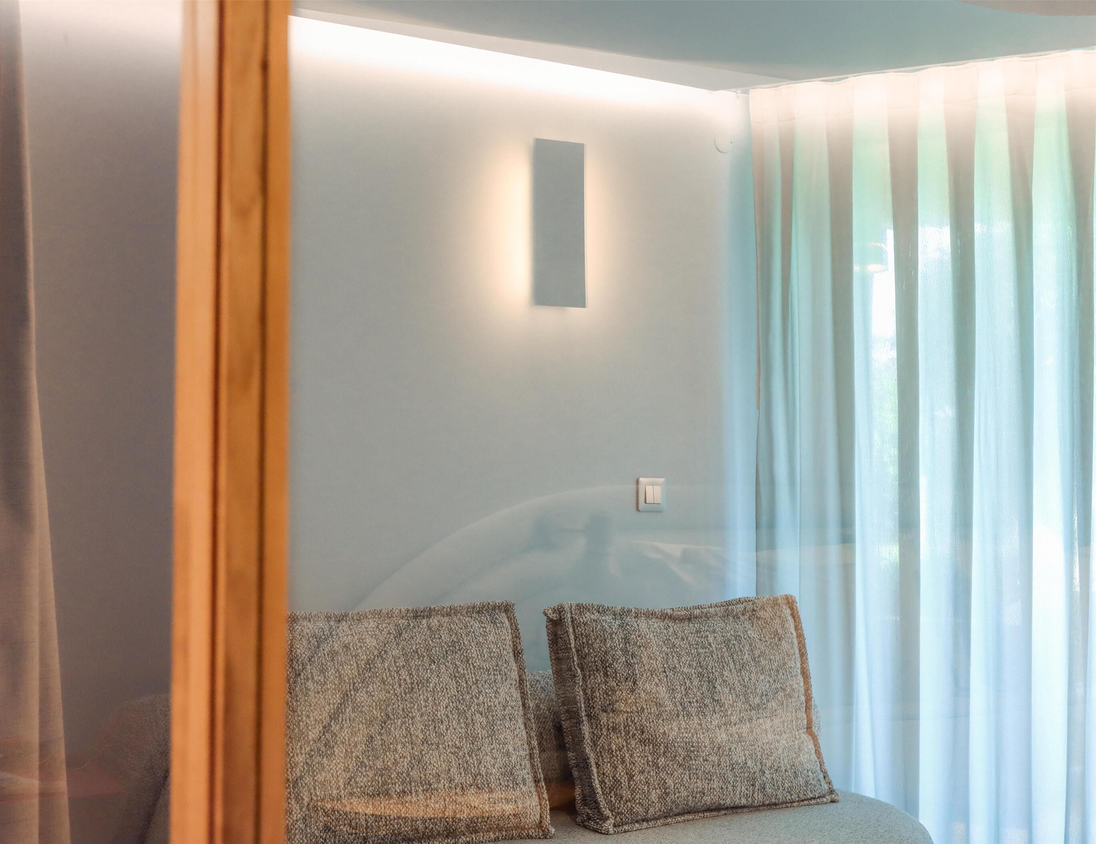 A room with a light blue wall, a wooden door, and a window with sheer curtains. There are two textured pillows on a light-colored sofa.