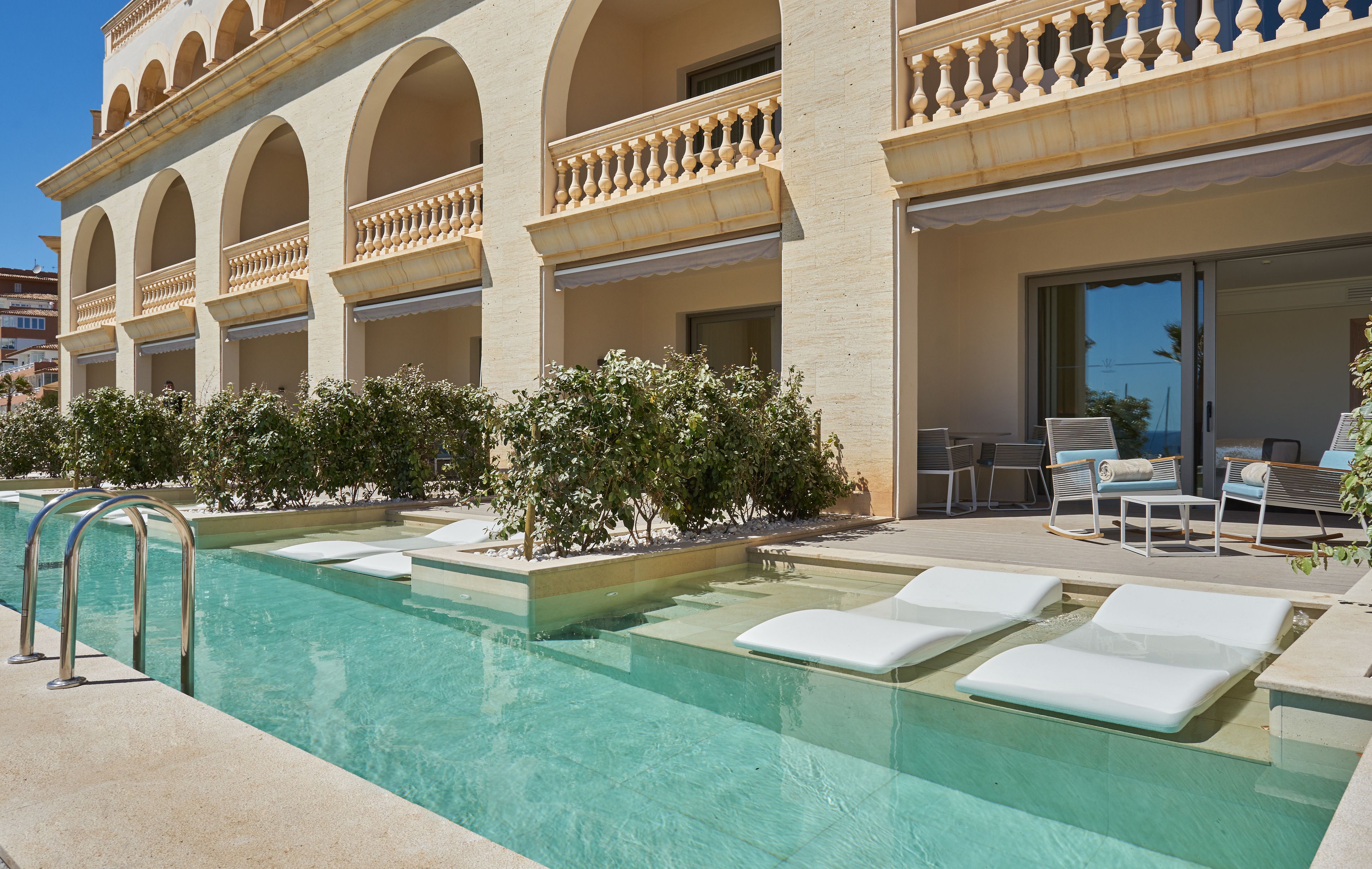 Un espace piscine avec des chaises longues et un bâtiment doté de fenêtres en arc de cercle et de balcons.