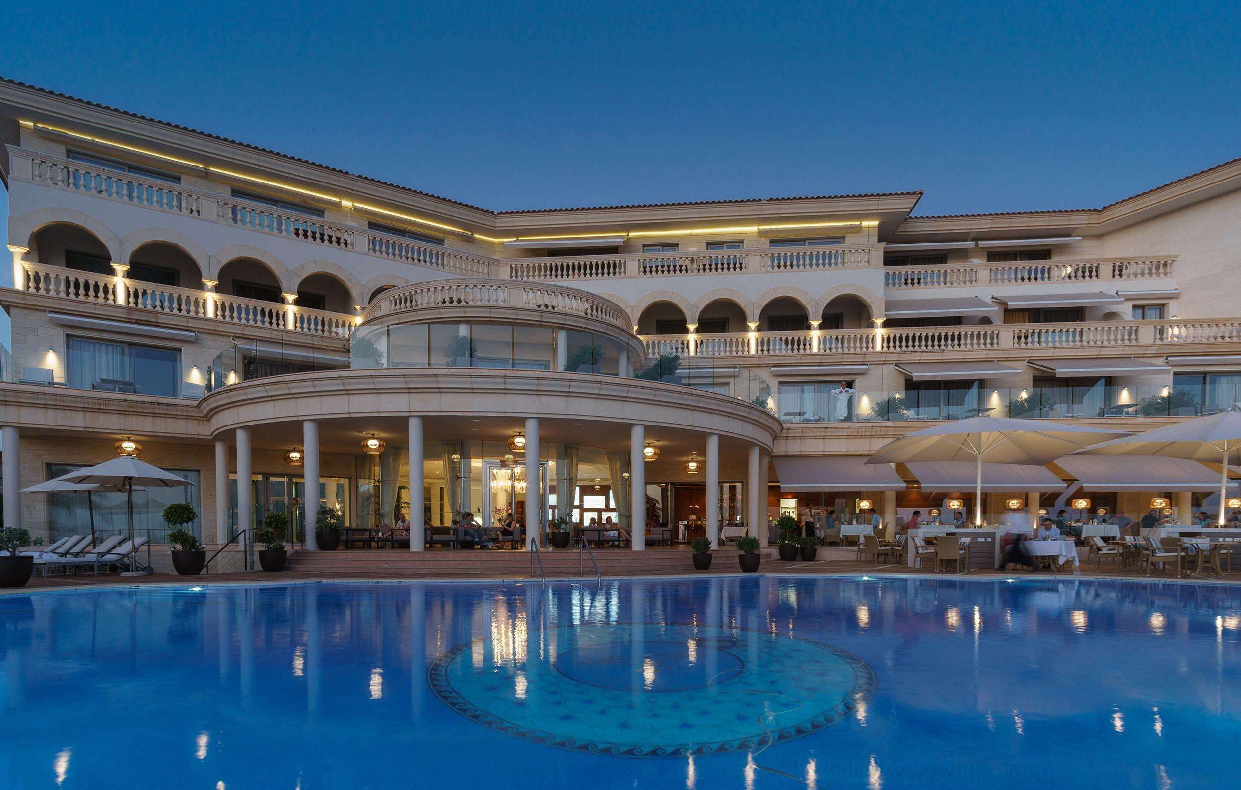 A large hotel with a central pool, multiple balconies, and outdoor seating areas.