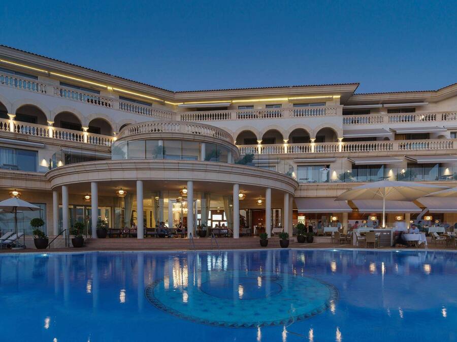A large hotel with a central pool, multiple balconies, and outdoor seating areas.