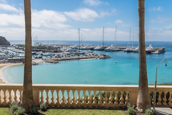 Un puerto deportivo con varios yates amarrados, un cielo azul despejado y vistas a la costa.