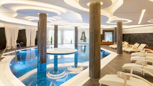 A modern indoor pool area with a central circular pool, surrounded by lounge chairs and large wooden pillars. - Pure Salt Port Adriano Hotel & SPA - Adults Only (Calvia)