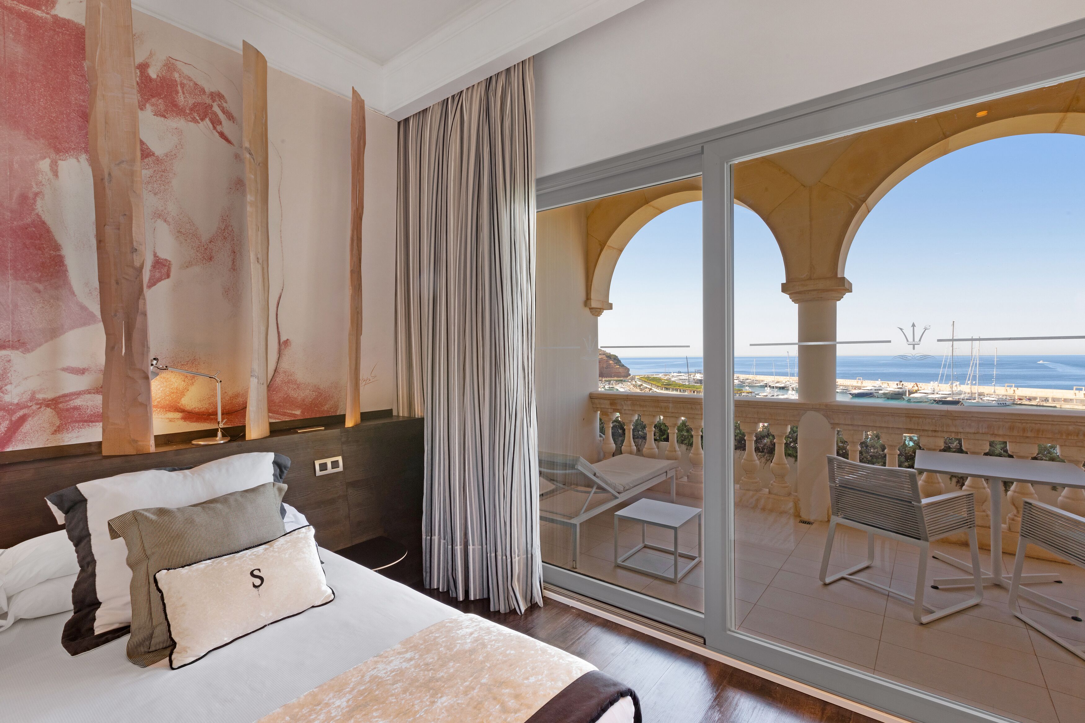 Un dormitorio con una cama grande, vista al mar y un balcón con mobiliario exterior.