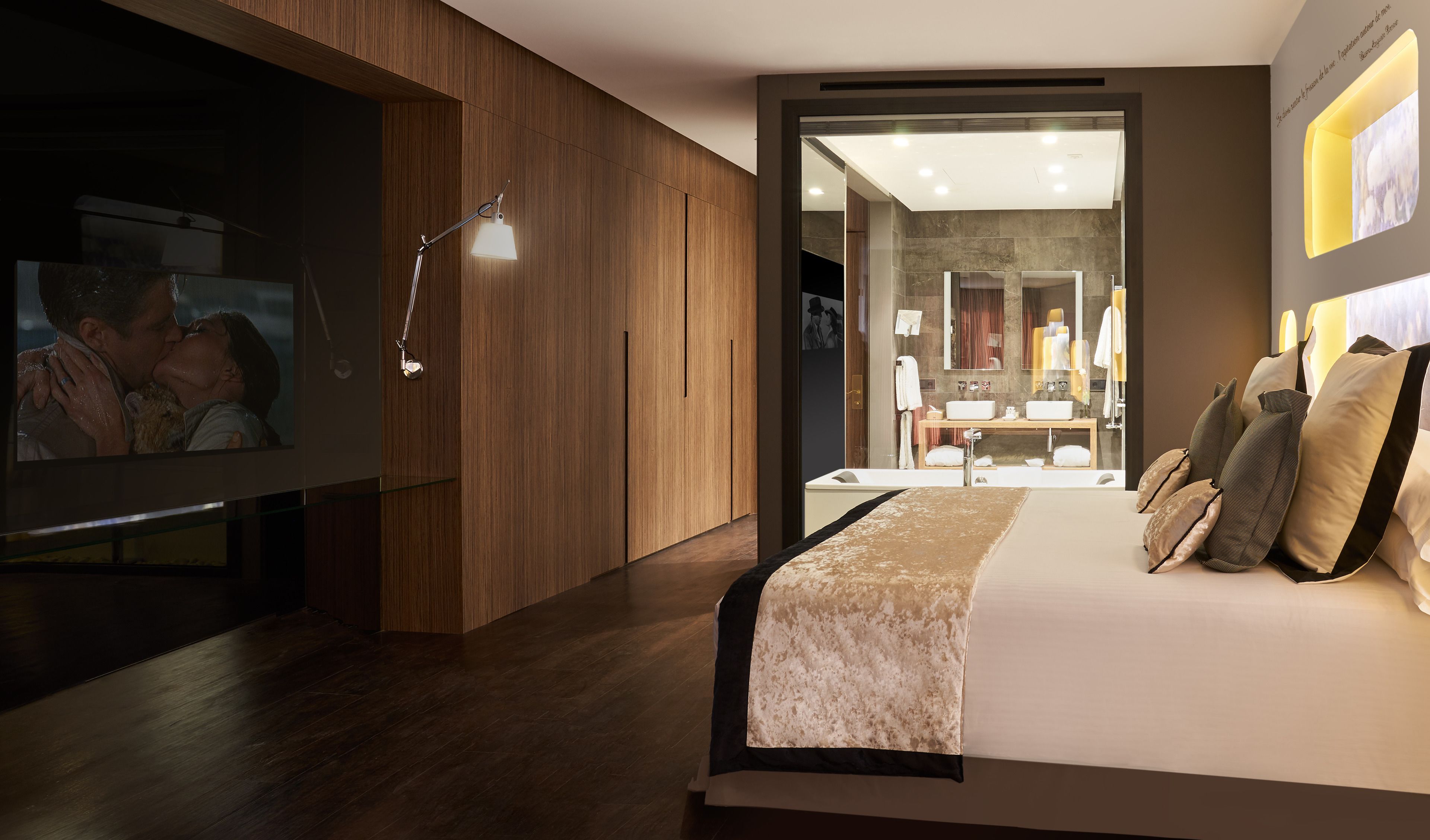 Un dormitorio moderno con una cama grande, un televisor y un baño visible a través de una puerta abierta.