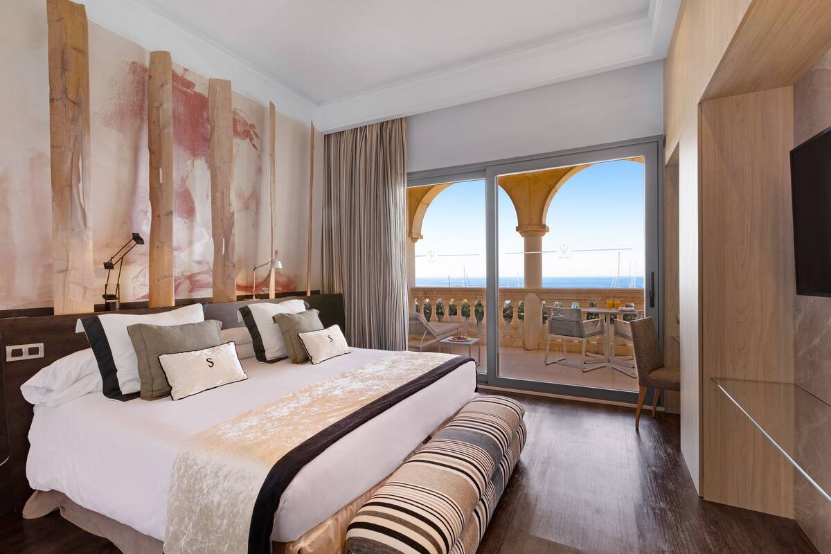 A modern hotel room with a large bed, a balcony with a view, and a dining area.