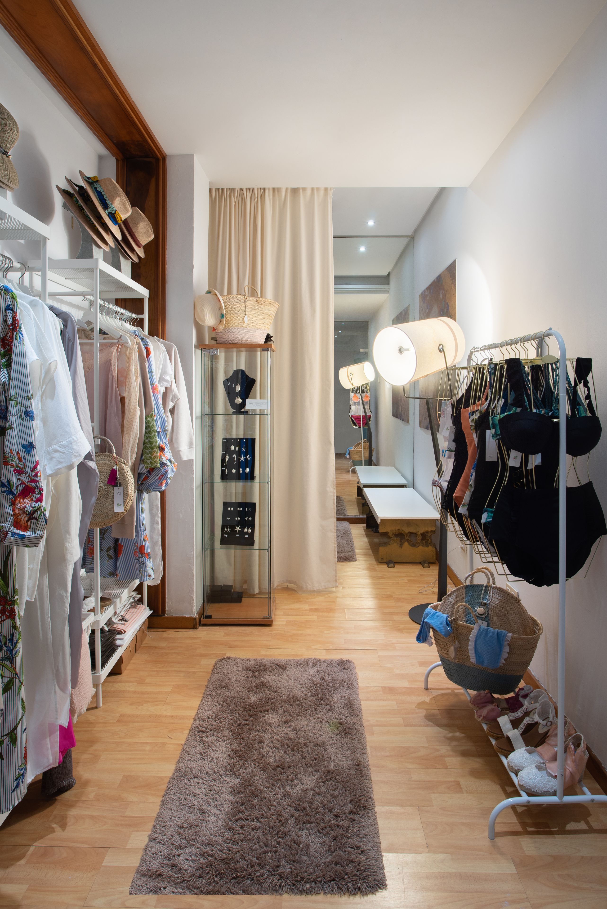 Une chambre d’hôtel de style boutique, bien aménagée, avec un plancher en bois, une grande fenêtre avec des rideaux, un tapis gris confortable et divers articles de vêtements disposés sur des portants et des étagères.