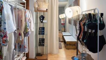 Habitación de hotel boutique bien organizada, con piso de madera, un ventanal con cortinas, un tapete gris acogedor y varios artículos de ropa en percheros y estantes.