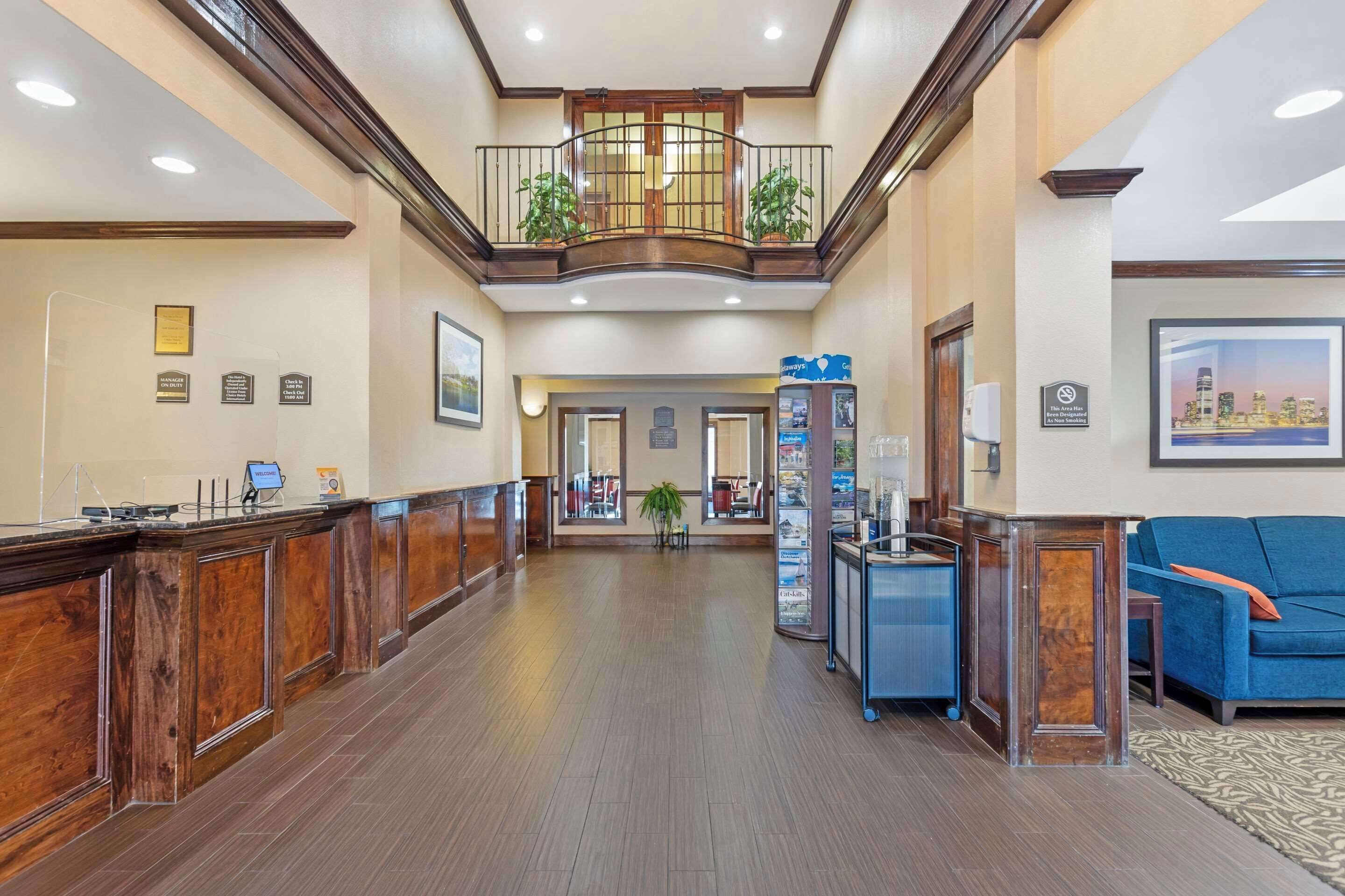 A spacious lobby with a wooden reception desk, a blue sofa, and a balcony with plants.