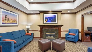 A hotel lobby with a blue sofa, ottomans, a fireplace, and framed pictures on the walls. - Comfort Inn & Suites Carneys Point - Pennsville (Penns Grove)