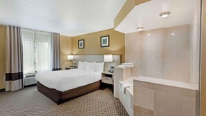 A hotel room with a large bed, a bedside table with a lamp, a bathroom with a bathtub, and a window with curtains. - Comfort Inn & Suites Carneys Point - Pennsville (Penns Grove)