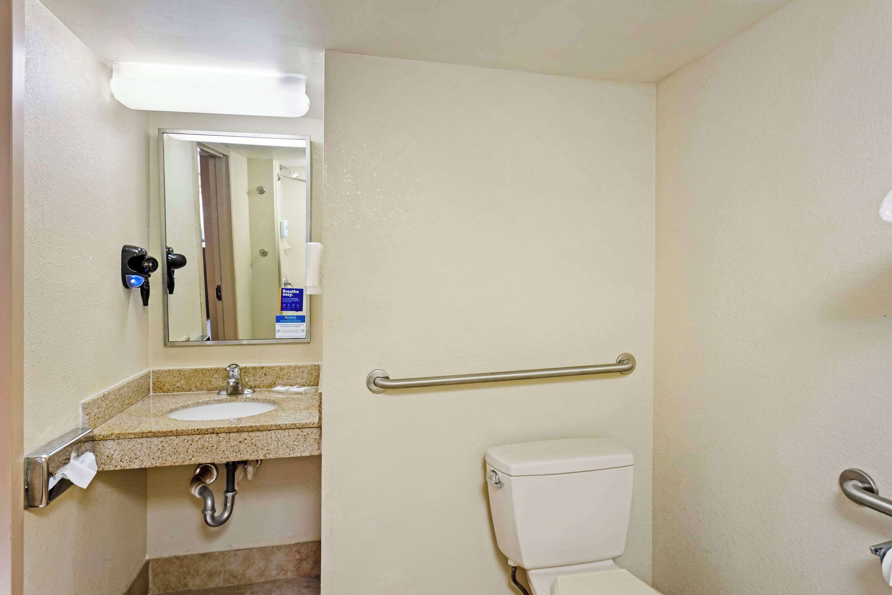 A bathroom with a sink, mirror, towel dispenser, and toilet.