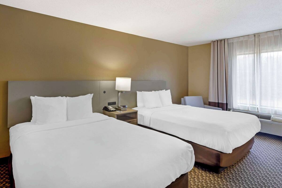 A hotel room with two beds, a nightstand with a lamp, and a window with curtains.