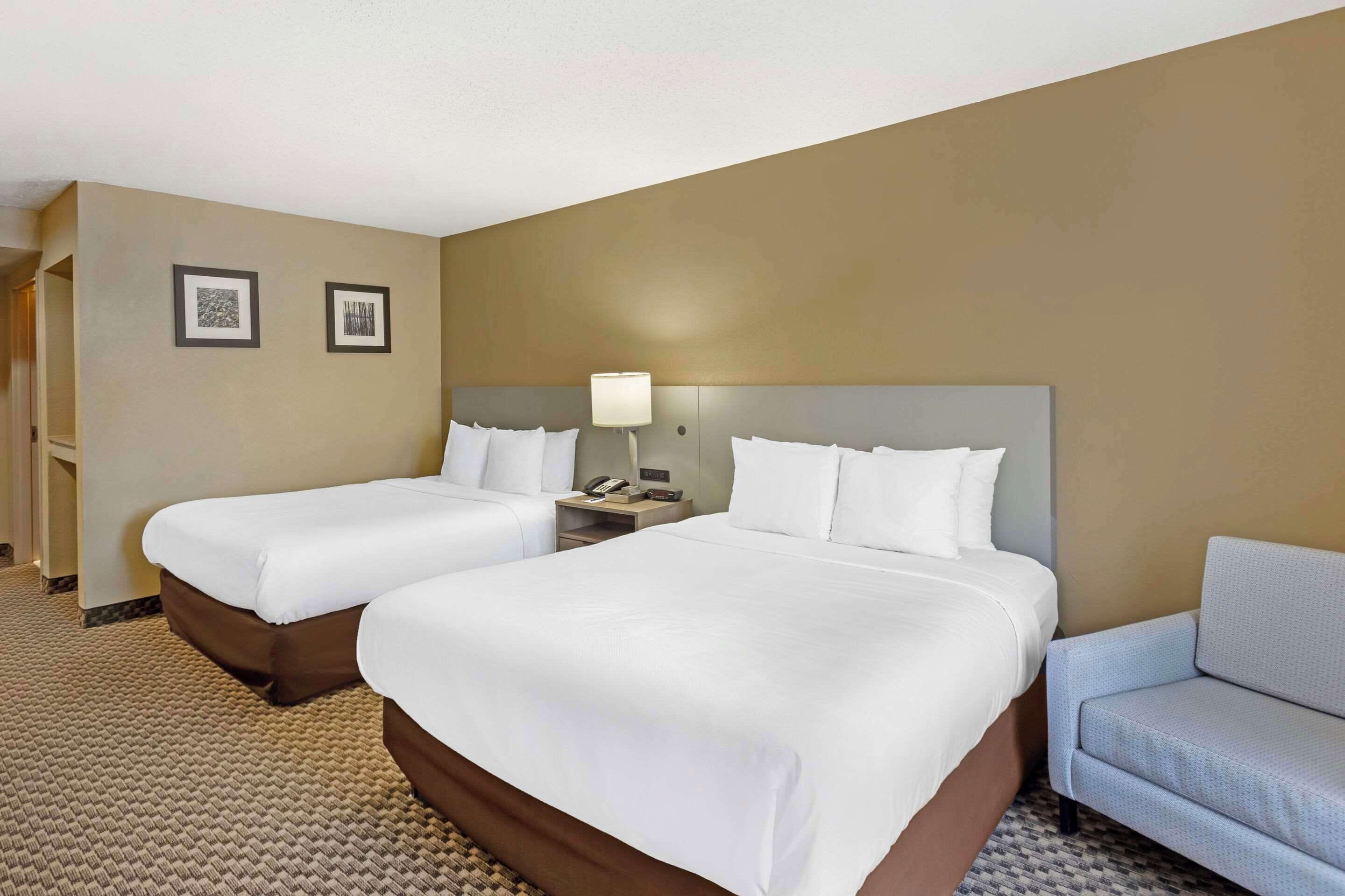A hotel room with two beds, a sofa, a nightstand with a lamp, and two framed pictures on the wall.