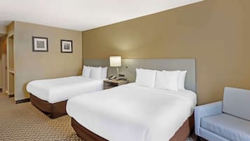 A hotel room with two beds, a sofa, a nightstand with a lamp, and two framed pictures on the wall.