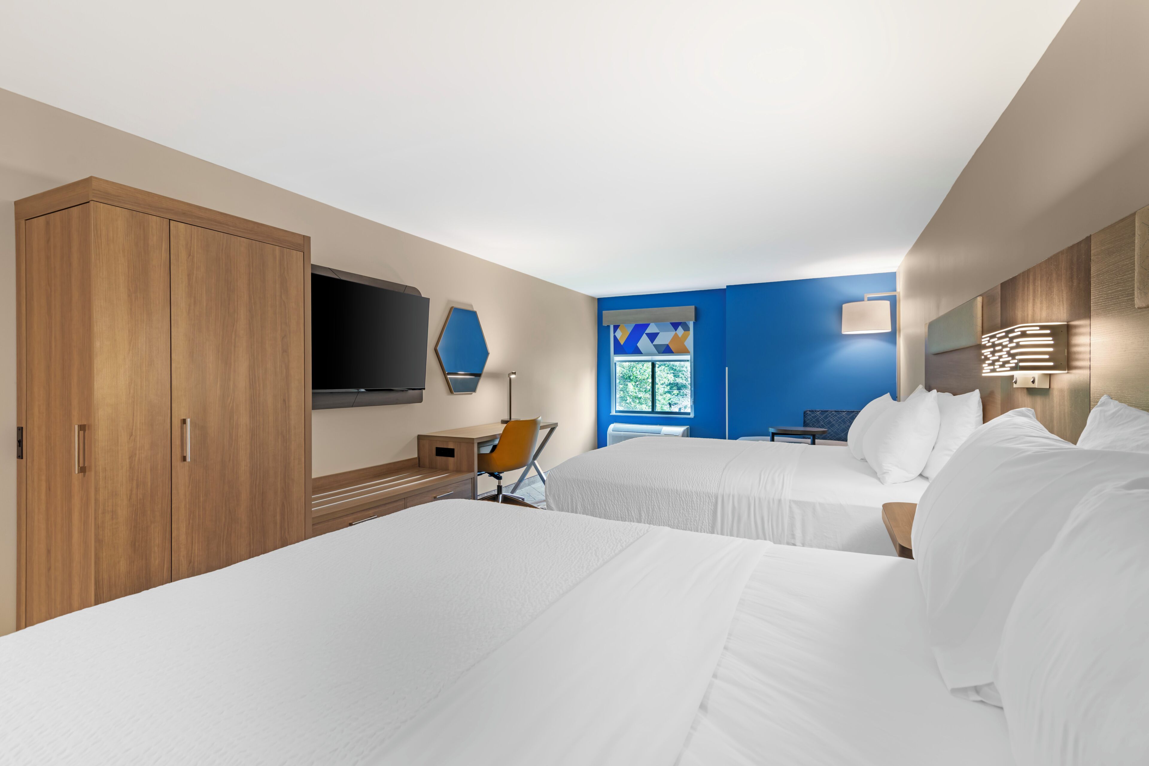 Habitación de hotel con dos camas, un escritorio, una silla, un televisor y una ventana con vistas.