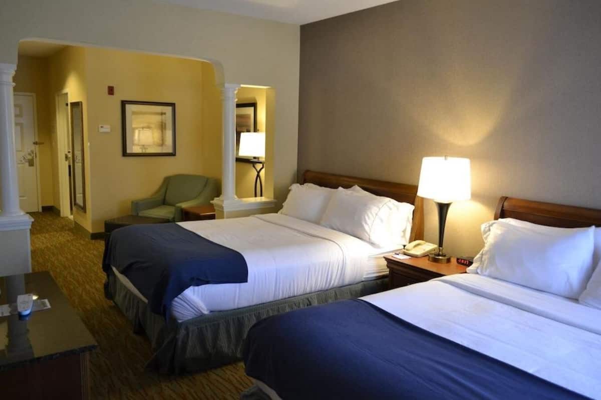 A hotel room with two beds, a desk, a chair, a lamp, and a framed picture on the wall.