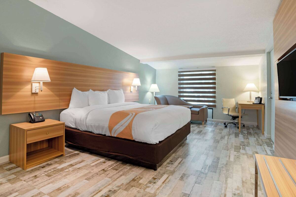 Quarto de hotel com cama grande, luminárias de cabeceira, escrivaninha e televisão.