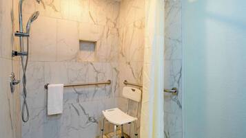 Un bagno con pareti in marmo, una doccia con soffione manuale, una barra di sostegno e un piccolo sgabello.