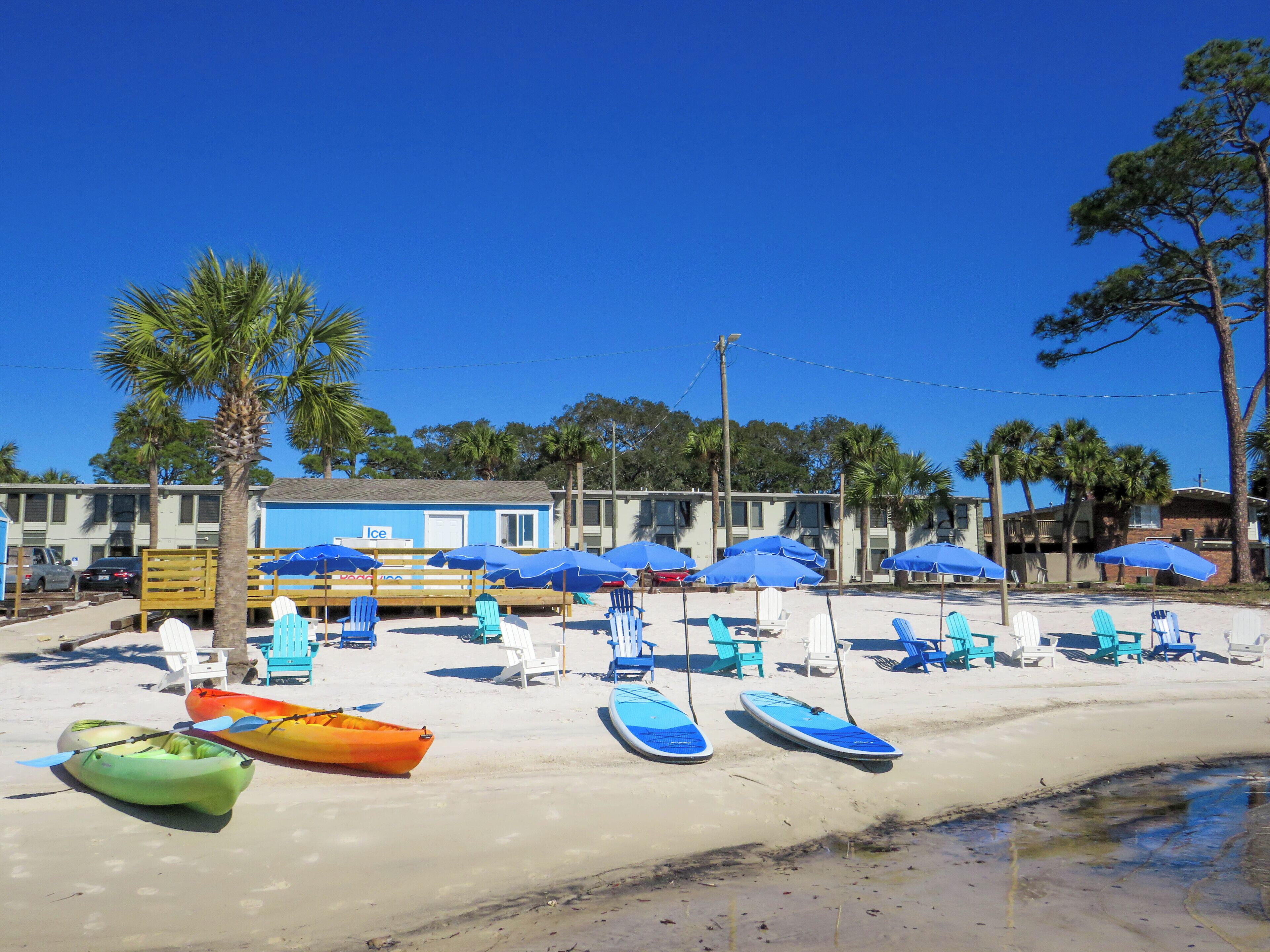 A beachside hotel with a pool area, kayaks, and beach chairs.