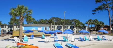 A beachside hotel with a pool area, kayaks, and beach chairs.